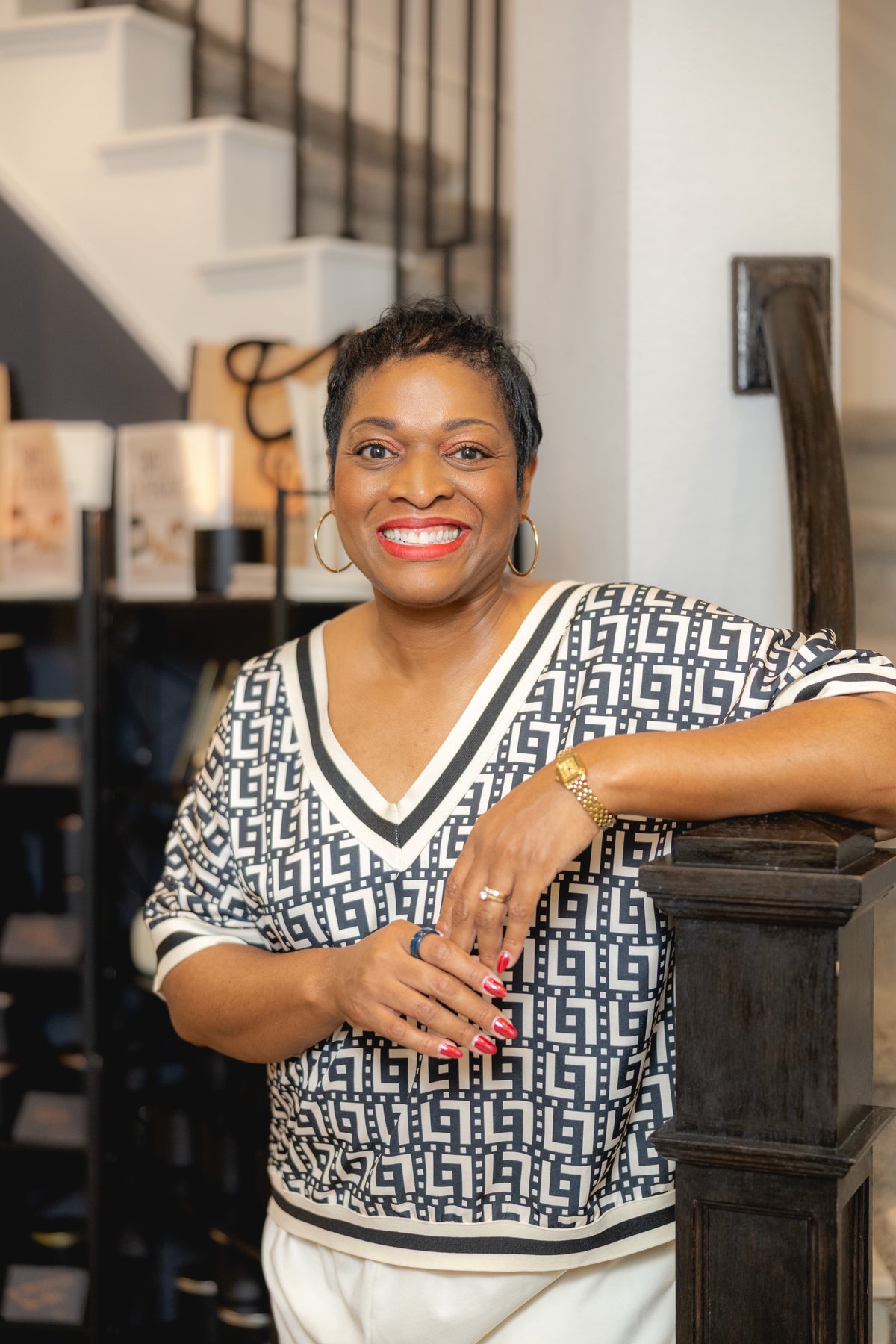 Gwendolyn Golden, founder of Gwen’s Gifts, smiling and leaning on a stair post in front of a shelf of candles